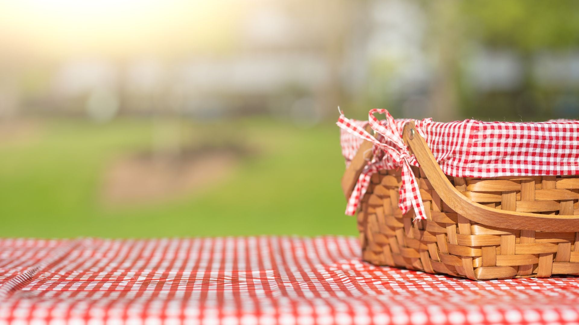 A wicker picnic basket on a red picnic blanket 